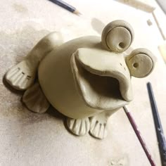 a clay fish with eyes and nose sitting on top of a table next to paintbrushes