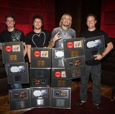 four men standing in front of a display of cd's on a red carpeted floor