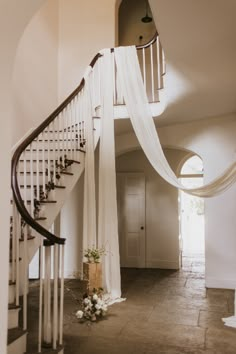 a staircase with white drapes and flowers on the bottom, next to a door