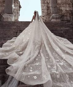 a woman in a wedding dress is standing on some stairs with her veil flowing over her head