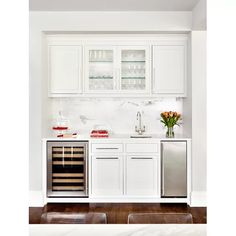 a white kitchen with stainless steel appliances and wine glasses on the cabinet doors, in front of a marble wall