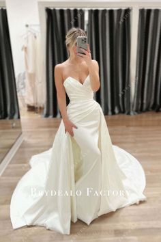 a woman in a wedding dress taking a selfie with her cell phone while standing on the floor