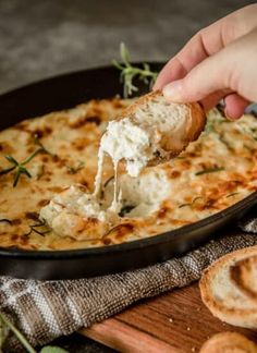 a person dipping some food into a skillet with garlic bread and herbs on the side