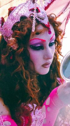 a woman with red hair and makeup is holding a mirror