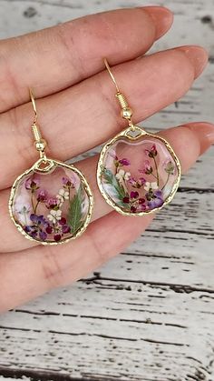 a hand holding a pair of earrings with flowers on it