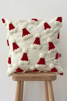 a white pillow with red and white santa hats on it, sitting on a wooden stool