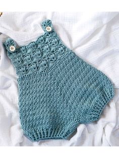 a blue crocheted baby romper laying on top of a bed next to a ball of yarn