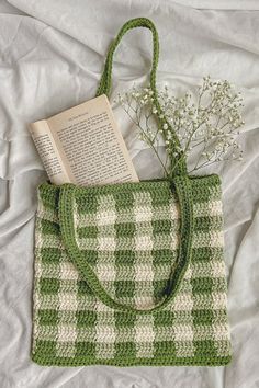 a green and white bag with a book on top of it next to some flowers