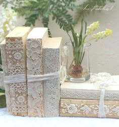 three books with lace on them sitting next to a vase filled with flowers and greenery