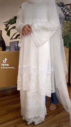 a woman wearing a white dress and veil in front of a wooden floor with plants