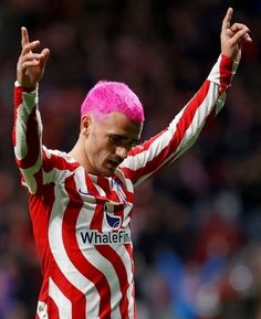 a soccer player with pink hair on his head and hands up in the air,