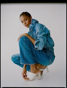 a woman sitting on top of a white chair wearing blue jeans and high heeled sandals