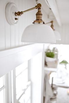 a white light hanging from the side of a wall next to a potted plant