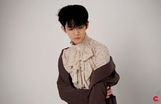 a young man with black hair wearing a brown and white scarf over his shoulders, standing in front of a gray background