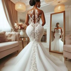 a woman in a white wedding dress looking at herself in the mirror with her back to the camera