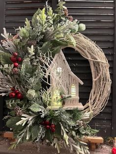 a wreath with a birdhouse on it and greenery around the wreath is sitting in front of a black door