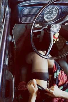 a woman sitting in the driver's seat of an old car holding a cell phone