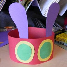 a paper crown with purple and green ears on top of a table next to books