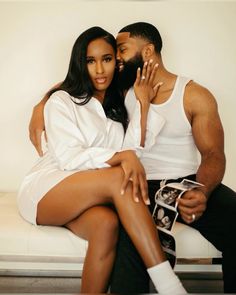 a man sitting next to a woman on a white couch in front of a wall