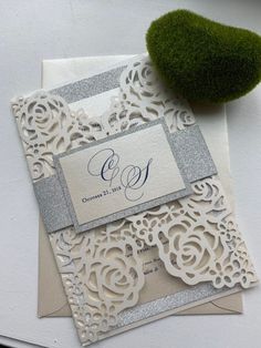 an elegant wedding card with silver glitters and lace on it, sitting next to a green plant