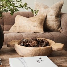 a wooden bowl filled with pine cones sitting on top of a table next to a book