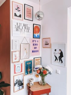 there is a wall with many pictures on it and a vase full of flowers in the corner