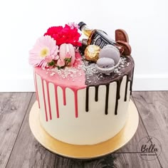 a cake decorated with flowers and chocolates on a wooden table next to a white wall