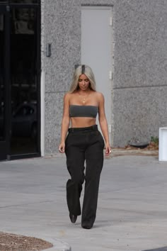 a woman walking down the street wearing black pants and a grey cropped tank top