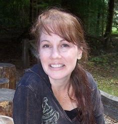 a woman sitting at a picnic table with food in front of her and smiling for the camera