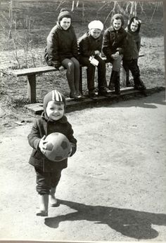 a young boy holding a soccer ball while standing in front of other children on a bench