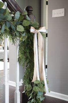 the wreath is tied up on the banister with ribbon and greenery around it