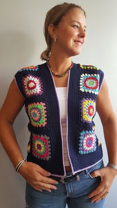 a woman standing in front of a white wall wearing a crocheted vest and smiling