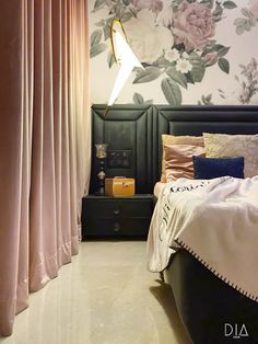 a bedroom with floral wallpaper and pink drapes on the windowsill, along with a black bed