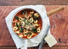 a bowl of pasta and spinach soup on a napkin with a wooden spoon next to it