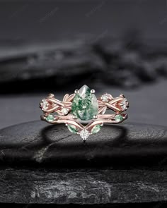 an engagement ring with green and white stones on top of a black stone slab in front of