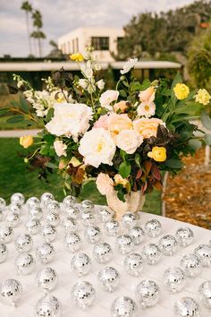 a vase filled with lots of flowers sitting on top of a white table covered in silver balls