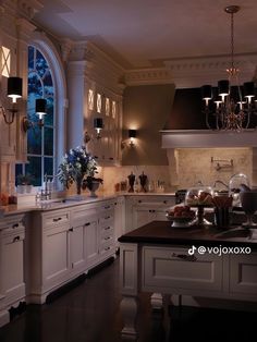 an elegant kitchen with white cabinets and black counter tops is lit by candle chandeliers