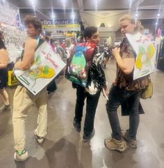 three people holding up signs in the middle of a convention hall with other people standing around