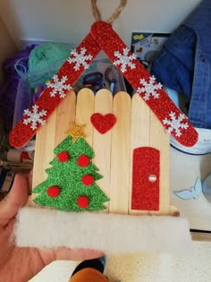 a hand holding up a wooden house shaped ornament with a christmas tree on it