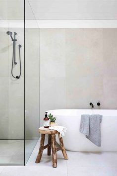 a white bath tub sitting next to a wooden stool in front of a walk in shower