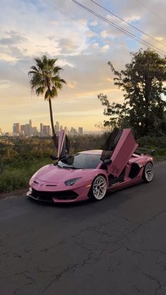 a pink sports car parked on the side of a road with its doors open in front of it