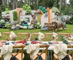 there are many hats on the tables at this outdoor birthday party that is decorated with dinosaurs and balloons