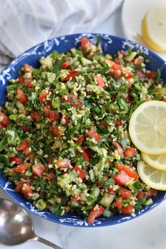 a blue bowl filled with salad and lemon wedges on top of a white table