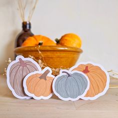 three paper pumpkins sitting on top of a table next to oranges and a bowl