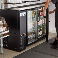 a woman standing in front of a cooler filled with bottles and drinks on top of a counter