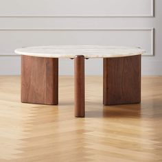 a white marble top coffee table with two wooden legs on a hard wood floor in an empty room