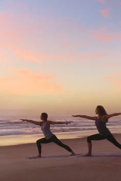 two women doing yoga on the beach at sunset