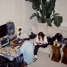 two people sitting on a couch in front of a table with computers and other electronic equipment