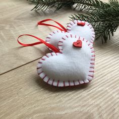 two ornaments hanging from a christmas tree on a wooden table with pine needles and red ribbon