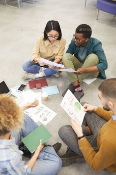 four people sitting on the floor looking at papers and folders - stock photo - images